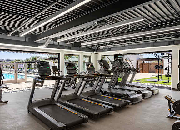 A gym with treadmills and a pool outside the window.