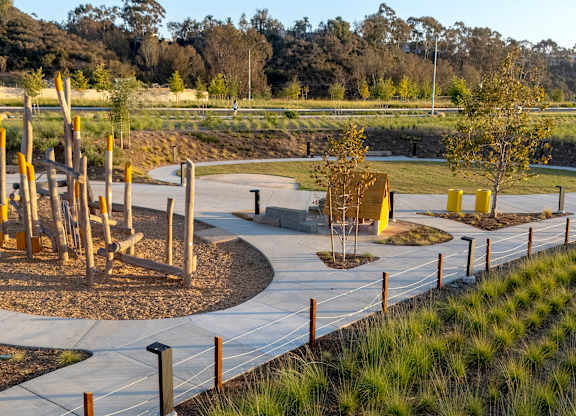 A playground with a wooden swing set and a concrete walkway.