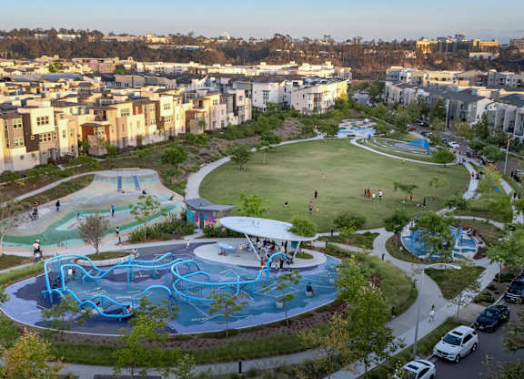 A playground with a blue slide and a white canopy is surrounded by a green lawn and trees.