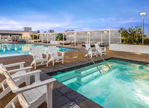 A rooftop spa area with a jacuzzi and chairs.