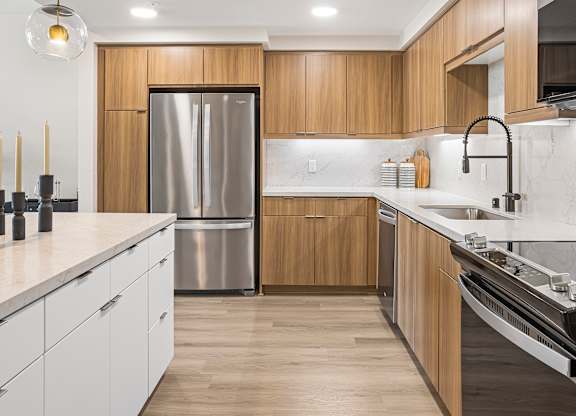 Bright apartment kitchen with wooden cabinets and stainless-steel appliances.