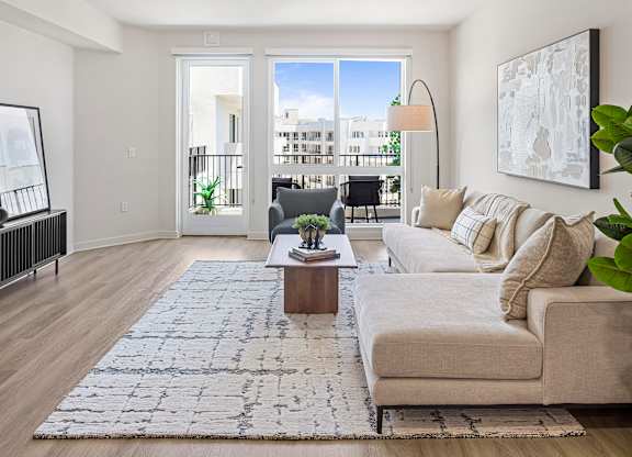A bright living room with a white couch, a coffee table, and a large window overlooking a balcony.