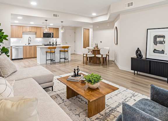 A modern living room with a grey sofa, a wooden coffee table, and a kitchen area in the background.