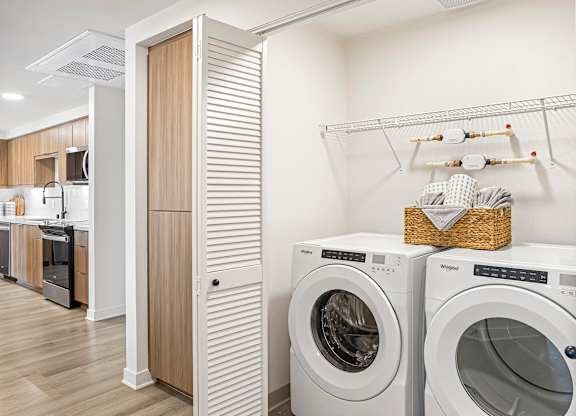 A laundry room with a washer and dryer, a basket of towels, and a wooden cabinet.