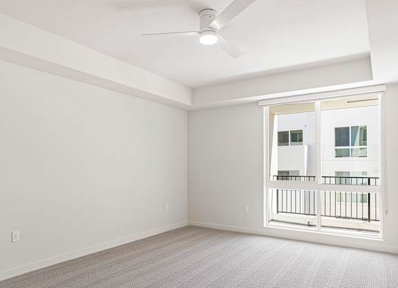 A bright room with a ceiling fan and a large window.