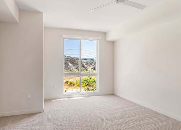 A room with a ceiling fan and a large window overlooking a landscape.