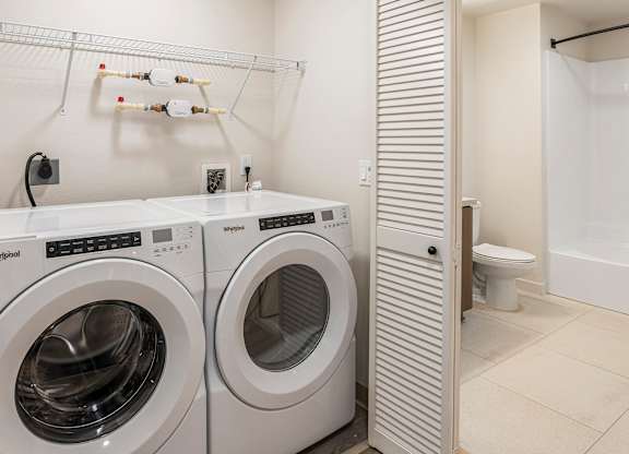 A laundry room with two front loading washing machines and a towel rack above them.