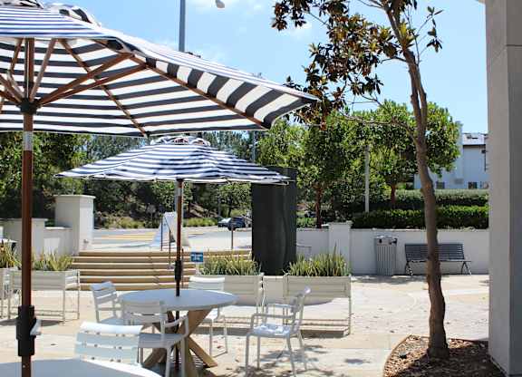 Outdoor patio with striped umbrellas and white chairs at Torrey Gardens Apartments, San Diego, California