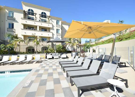 Poolside lounge deck with striped pavers and yellow umbrella at 360 Luxury Apartments, San Diego