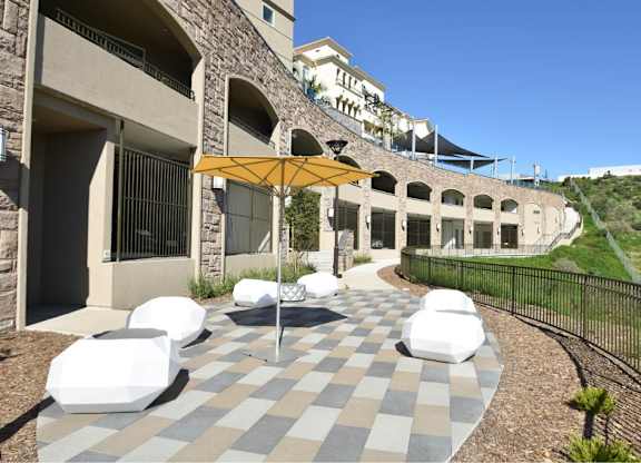 Patio seating area with yellow umbrella and white ottomans at 360 Luxury Apartments, San Diego, 92122