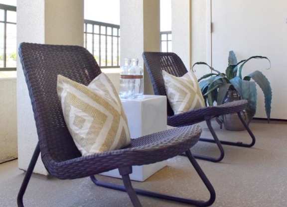 Covered balcony with wicker chairs and patterned pillows at 360 Luxury Apartments, San Diego