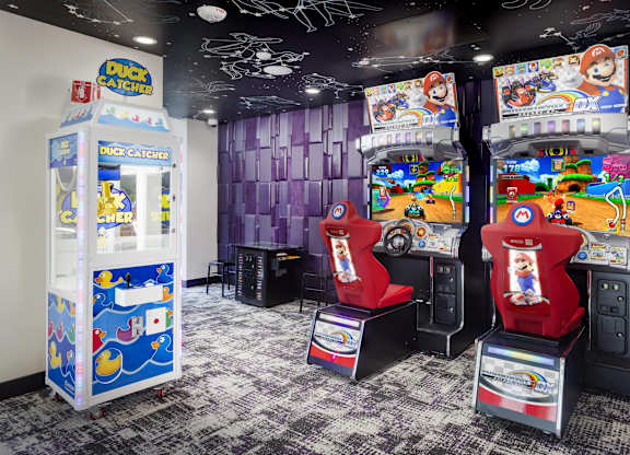 Arcade game room with racing simulators and claw machine at LUX by Garden* Apartments, California, 92122