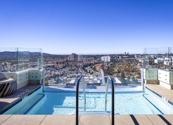 Rooftop infinity pool with glass railing and city skyline views at LUX by Garden* Apartments, San Diego, California