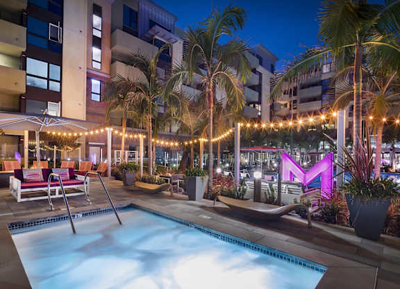 Evening poolside courtyard with string lights and palm trees at Metropolis Apartments, IRVINE, 92614