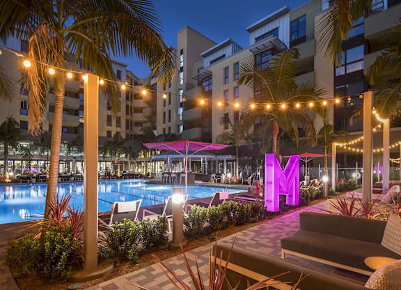 Pool deck with illuminated signage and lounge seating at Metropolis Apartments, IRVINE, California