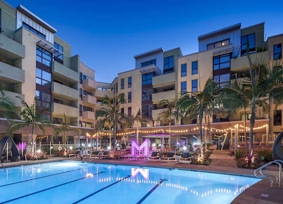 Twilight pool area with lit signage and tropical landscaping at Metropolis Apartments, IRVINE