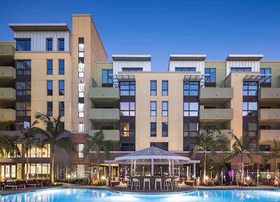 Illuminated swimming pool with courtyard dining pavilion at dusk at Metropolis Apartments, California