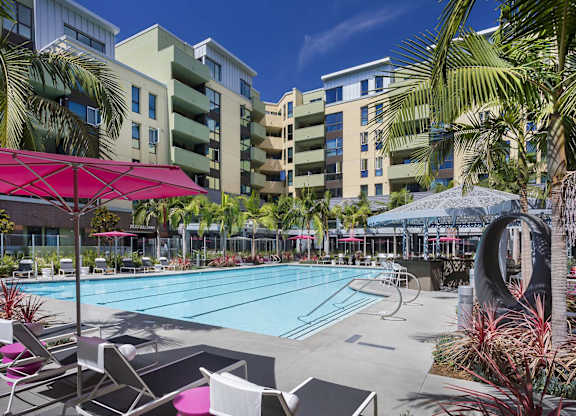Resort style pool with pink umbrellas and palm trees at Metropolis Apartments, IRVINE, CA 92614
