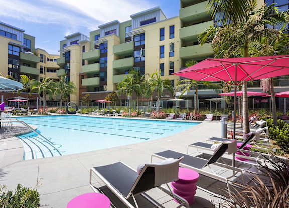 Swimming pool with modern lounge chairs and pink umbrellas at Metropolis Apartments, IRVINE, CA