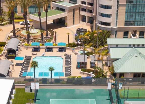 Tennis court surrounded by palm trees and buildings. at Towers at Costa Verde Apartments, San Diego, CA