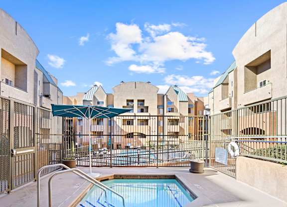 Hot tub with fenced pool area and shade umbrella at Costa Verde Village Apartments, San Diego, California