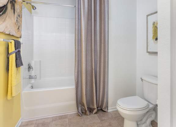 Bathroom with yellow towels and patterned curtain at Costa Verde Village Apartments, California
