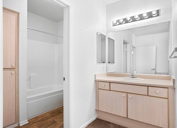 Bathroom with light wood vanity and large mirror at Costa Verde Village Apartments, San Diego