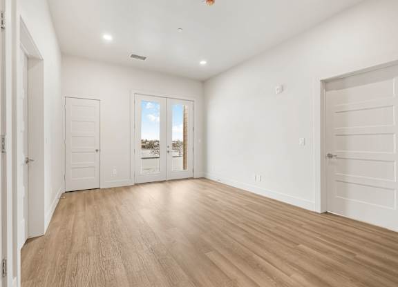 A room with white walls and wooden flooring, with a view of a building outside the window.