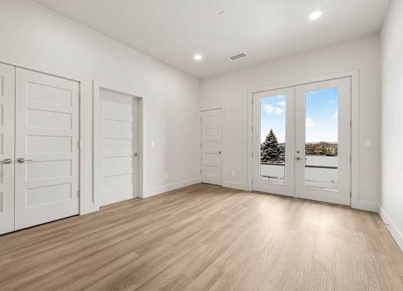 A room with white walls and wooden flooring, with a view of a tree through a window.
