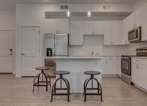A kitchen with white cabinets and a white island with two stools in front.