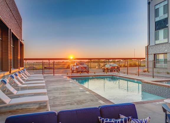 A sunset view from a rooftop pool area with lounge chairs and a fence.