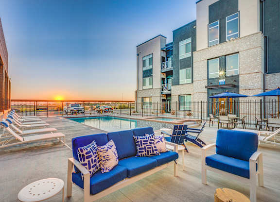 A sunset view of a pool area with a blue sofa and chairs.