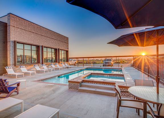 A sunset view of a pool area with lounge chairs and a building.