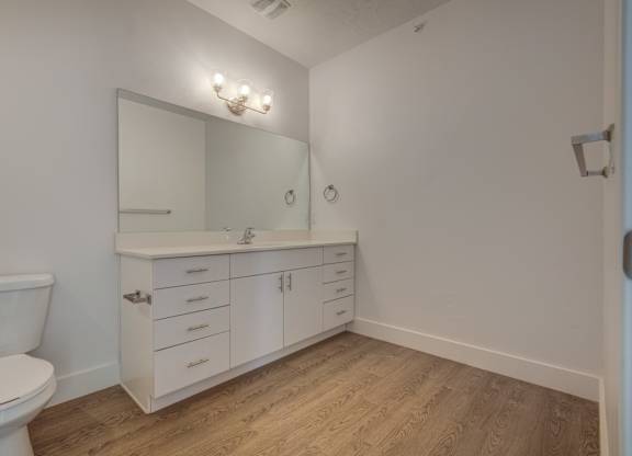 A white bathroom with a toilet, sink, and wood flooring.