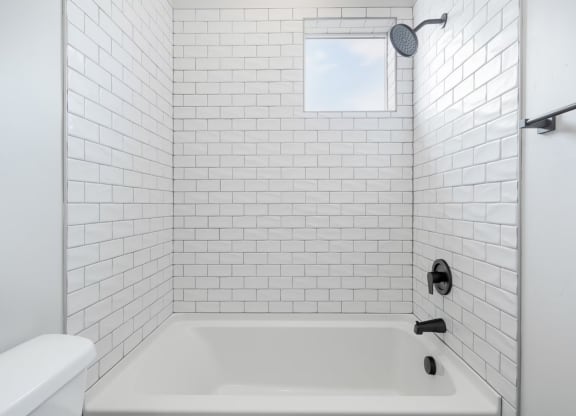 a white bathroom with white tiled walls and a white tub