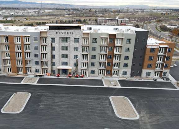 A large multi-story apartment building named Reverie sits in a parking lot.