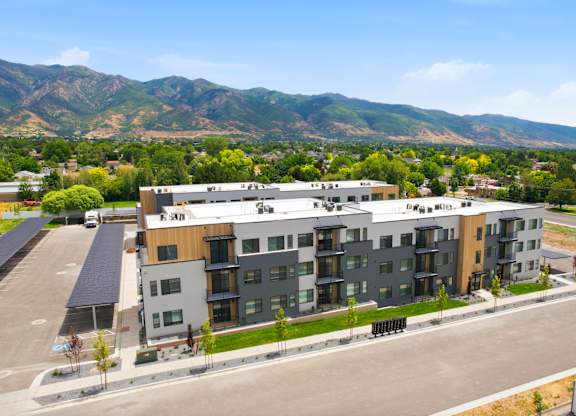 A modern apartment complex with a parking lot in front and mountains in the background.