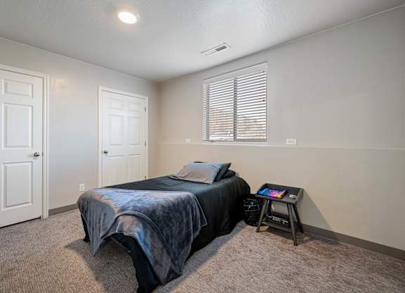 A bedroom with a bed, a table, and two doors.