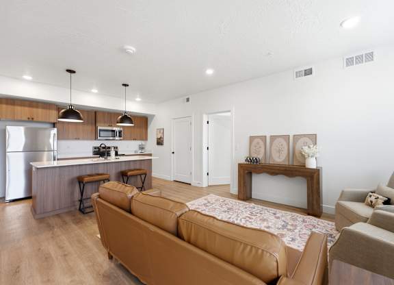 A modern living room with a brown sofa and a kitchen area in the background.