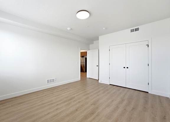 A room with white walls and wooden flooring with a white door on the right.