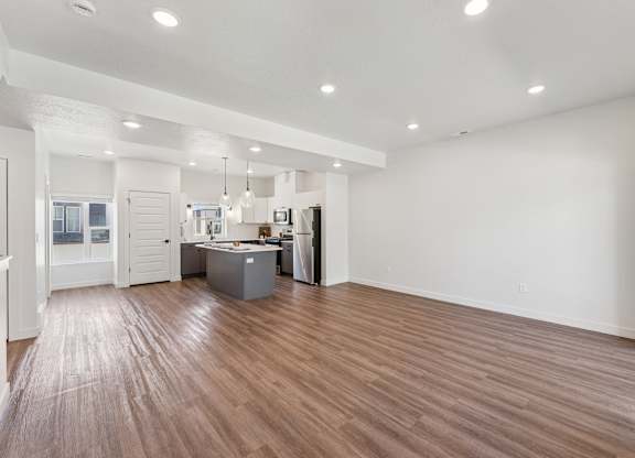 A spacious room with wooden flooring and a kitchen area in the background.