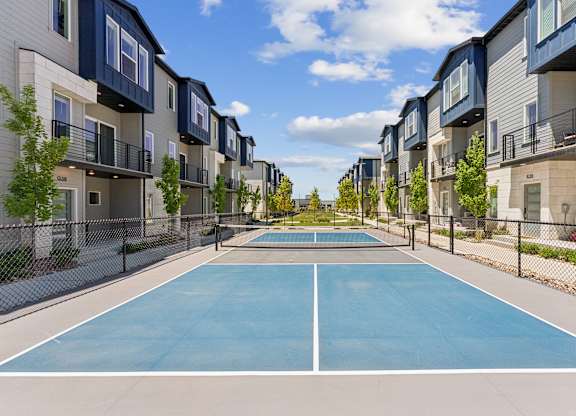 A tennis court is surrounded by apartment buildings.
