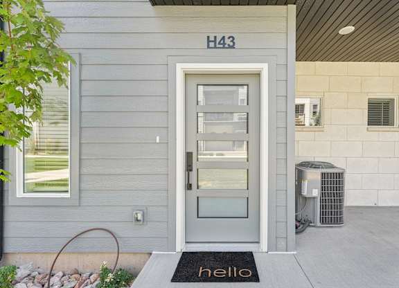 A grey door with a glass panel and a black mat that says hello in front of it.
