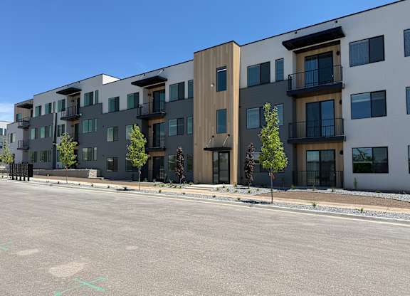 A row of modern apartment buildings with balconies and trees in front.