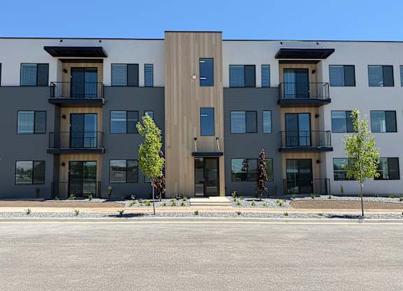 A modern apartment building with balconies and trees in front.