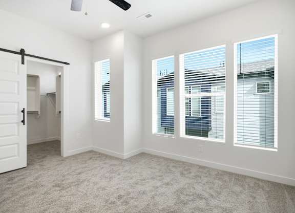 A room with a carpet floor, a ceiling fan, and three windows.
