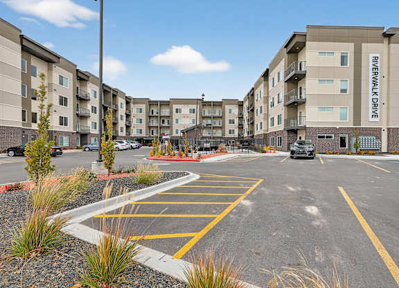 A parking lot in front of apartment buildings with a car parked in the lot.