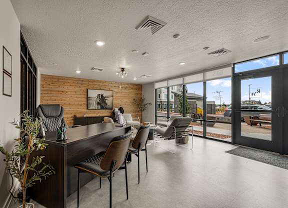 A modern office space with a long table and chairs, a brick wall, and a view of the outdoors.