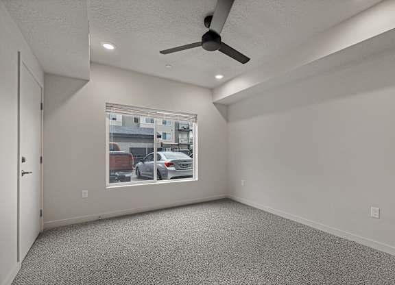 A room with a ceiling fan and a window showing a parking lot outside.