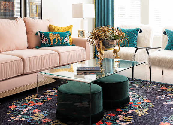 A living room with a pink couch, a glass coffee table, and a floral rug.